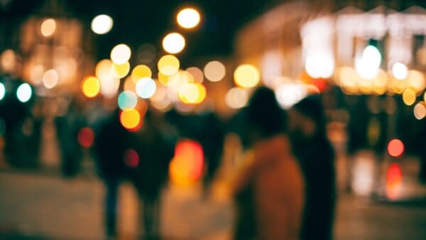 Blurry city street at night with colorful bokeh and silhouettes of people.